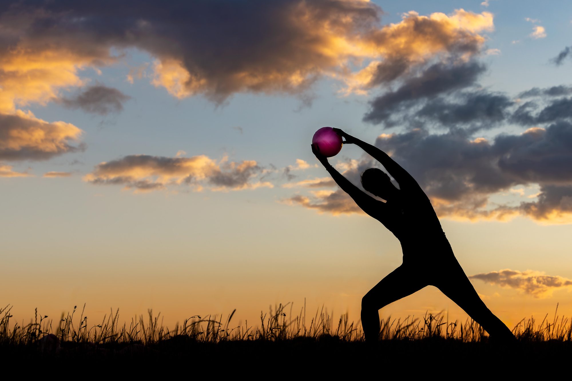 A person stretching with a pilates ball against a golden sunset sky
